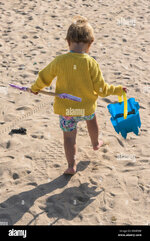 a-toddler-carrying-her-bucket-and-spade-walking-on-a-beach-K0NF2M.jpg